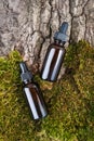 Two brown glass bottles and pipette whith serum, essential oil on green moss and tree bark background. Natural Organic