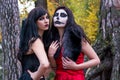 Two brunettes women with makeup like a Halloween skull and Halloween witch makeup stands in a red and black dresses in the autumn
