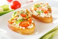 Two Bruschetta with red sweet pepper and goat cheese in a plate next to fresh vegetables on white boards. Royalty Free Stock Photo