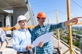 Two Builders On Construction Site Looking At Plans Contractor Meeting With Business Man