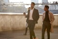 Two business colleagues walking by the Thames riverside in the city of London talking, man holding takeaway coffee Royalty Free Stock Photo