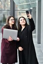 Two business girls take a selfie on the phone, work on a laptop on the background of the office, on the street Royalty Free Stock Photo