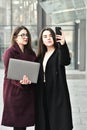 Two business girls take a selfie on the phone, work on a laptop on the background of the office, on the street Royalty Free Stock Photo