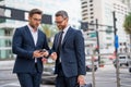 Two business men using mobile phone app texting outside of office in urban city. Businessmen holding smartphone for Royalty Free Stock Photo