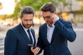 Two business men using mobile phone app texting outside of office in urban city. Businessmen holding smartphone for Royalty Free Stock Photo