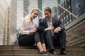 Two business partnership being cheerful sitting and watching tablet computer outdoors in city