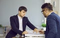 Two business people in office sign contract sitting at desk, manager gives document to his client. Royalty Free Stock Photo