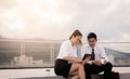 Two business people sitting on roof floor and using digital tablet at outside business office together