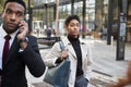 Two business people walking in a street in the city of London, man using smartphone and woman carrying a bag, selective focus Royalty Free Stock Photo