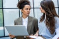 Two business people, working women, smiling and looking at each other one holding laptop other plans and documents with statistics Royalty Free Stock Photo