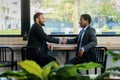 Two businessmen having handshaking by window in coffee shop