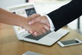 Two businessmen shake hands in an office with computers laptop, smartphone, document on their desks after reaching an agreement to