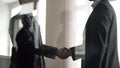 Two businessmen shaking hands to each other, confirming deal, view through glass
