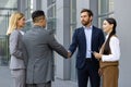 Two businessmen stand outside an office building together with female assistants, shake hands, greet each other when Royalty Free Stock Photo