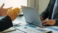 Two businessmen were analyzing a cost graph on a desk in a conference room with a laptop lit orange