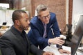 Two Businessmen Working At Computer On Desk In Open Plan Office