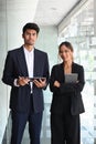 Two businesspeople holding digital tablet and looking at camera while standing in office lobby hall. Royalty Free Stock Photo