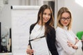 Two businesswomen coworkers standing in an office and smiling positively at the camera while holding folder of paperwork Royalty Free Stock Photo