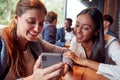 Two Businesswomen Looking At Photos On Mobile Phone In Bar After Work With Colleagues Royalty Free Stock Photo