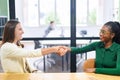 Two businesswomen sitting at the desk and shaking hands each other in sign of cooperation Royalty Free Stock Photo