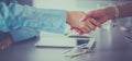 Two businesswomen sitting at a desk shaking hands