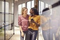 Two Businesswomen Standing In Corridor Of Modern Office Looking At Mobile Phone Royalty Free Stock Photo