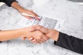 Two businesswomen wearing formal suits shake hands after making deal