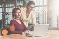 Two businesswomen working together. On desk is laptop. Woman is standing near table, girl is sitting next to her. Royalty Free Stock Photo