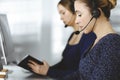 Two busineswomen have conversations with the clients by headsets, while sitting at the desk in a modern office. Diverse Royalty Free Stock Photo