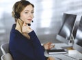 Two busineswomen have conversations with the clients by headsets, while sitting at the desk in a modern office. Diverse