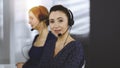 Two busineswomen have conversations with the clients by headsets, while sitting at the desk in a sunny modern office Royalty Free Stock Photo