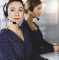 Two busineswomen have conversations with the clients by headsets, while sitting at the desk in a sunny modern office Royalty Free Stock Photo