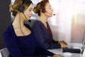 Two busineswomen have conversations with the clients by headsets, while sitting at the desk in a sunny modern office Royalty Free Stock Photo