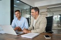 Two busy happy business men working together talking using laptop in office. Royalty Free Stock Photo