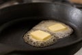 Two butter pats melting on a black cast iron frying pan. Royalty Free Stock Photo