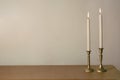 Two candles burning in vintage candlesticks on table against empty wall