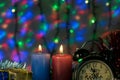 Two candles with clock and Christmas gifts with multi-colored lights on background