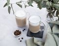 Two cappuccino or latte with milk foam in glasses on a light background with coffee beans and eucalyptus branch Royalty Free Stock Photo