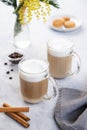 Two cappuccino or latte with milk foam in glasses on a light blue background with coffee beans, cinnamon and yellow mimosa flowers Royalty Free Stock Photo