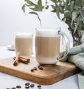 Two cappuccino or latte with milk foam in glasses on a wooden plate with coffee beans, cinnamon and eucalyptus branch close up. Royalty Free Stock Photo