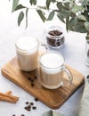 Two cappuccino or latte with milk foam in glasses on a wooden plate on a light background with coffee beans, cinnamon and Royalty Free Stock Photo