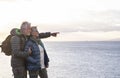 Two carefree senior people with backpack on their back enjoys the hike on the ocean cliffs looking at the horizon over water Royalty Free Stock Photo