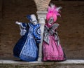 Two carnival-goers wearing brightly colored masks and costumes at Venice Carnival.