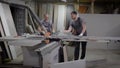 Two carpenters are working in a joiners shop in plant, cutting particle board for preparing for producing furniture