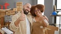 Two carpentry partners beaming, giving okay sign while hugging inside their woodworking workshop Royalty Free Stock Photo