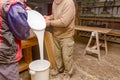 Two carpentry workers pour wood glue from a large plastic bucket into another empty