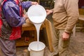 Two carpentry workers pour wood glue from a large plastic bucket into another empty