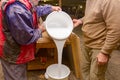 Two carpentry workers pour wood glue from a large plastic bucket into another empty