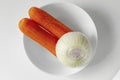Two Carrots and one onion without peel on white plate. Top view fresh vegetable ingredients set for making vegan soup or Royalty Free Stock Photo