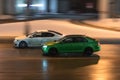 Two cars in motion on city street at night. Racing at high speed on public road. White and green sedans drive on wet winter road Royalty Free Stock Photo